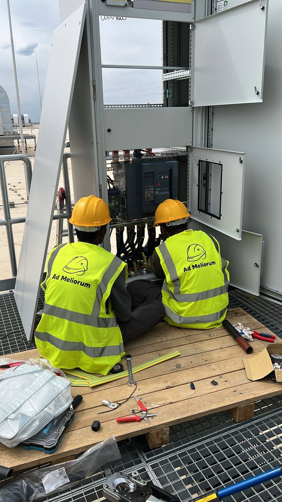 Two Ad Meliorum workers connecting a switchgear cabinet on a rooftop